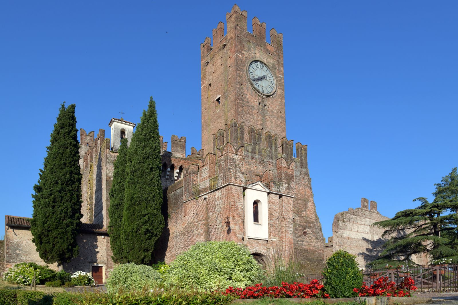 Majestic medieval castle with a clock tower surrounded by cypress trees in Italy.