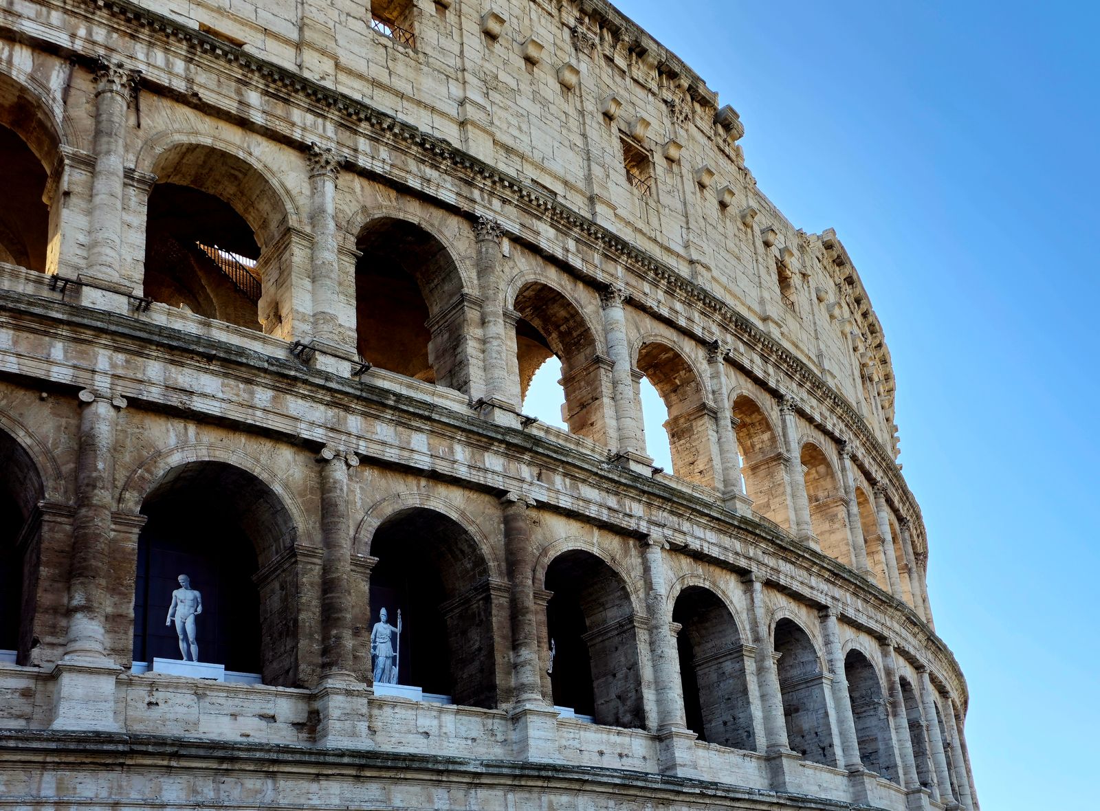 Side view of Rome's iconic Colosseum with clear blue sky.