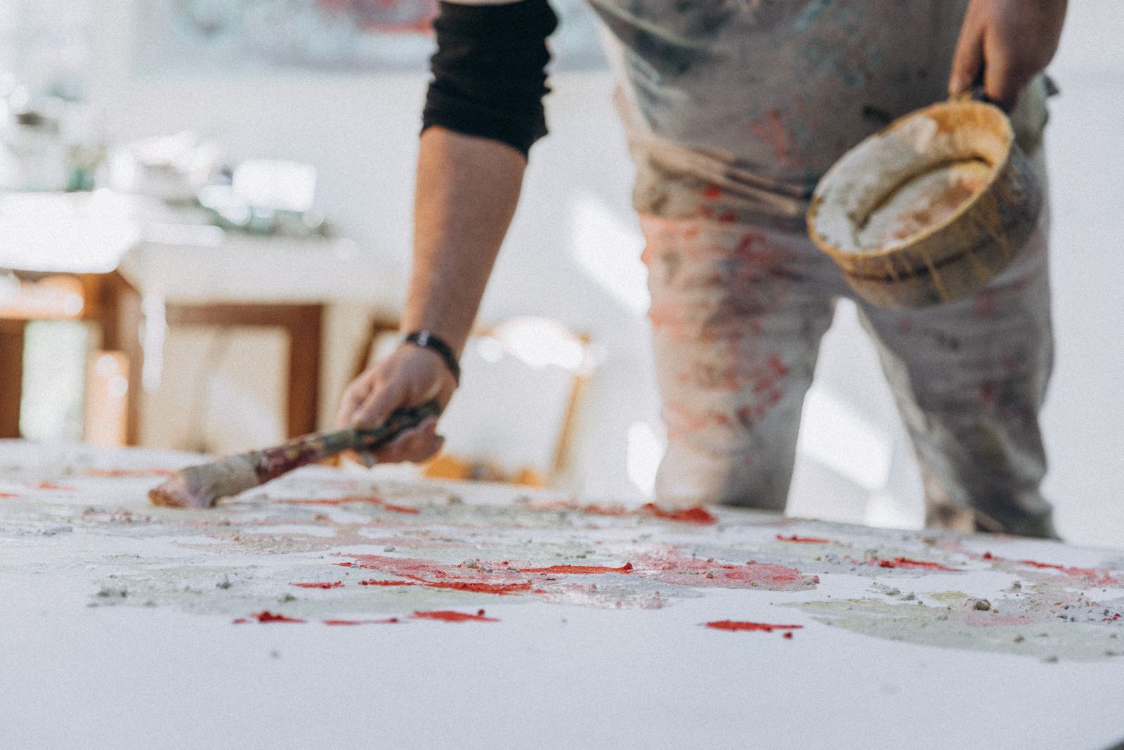 A focused painter applying colorful brushstrokes on a large canvas in a bright studio.