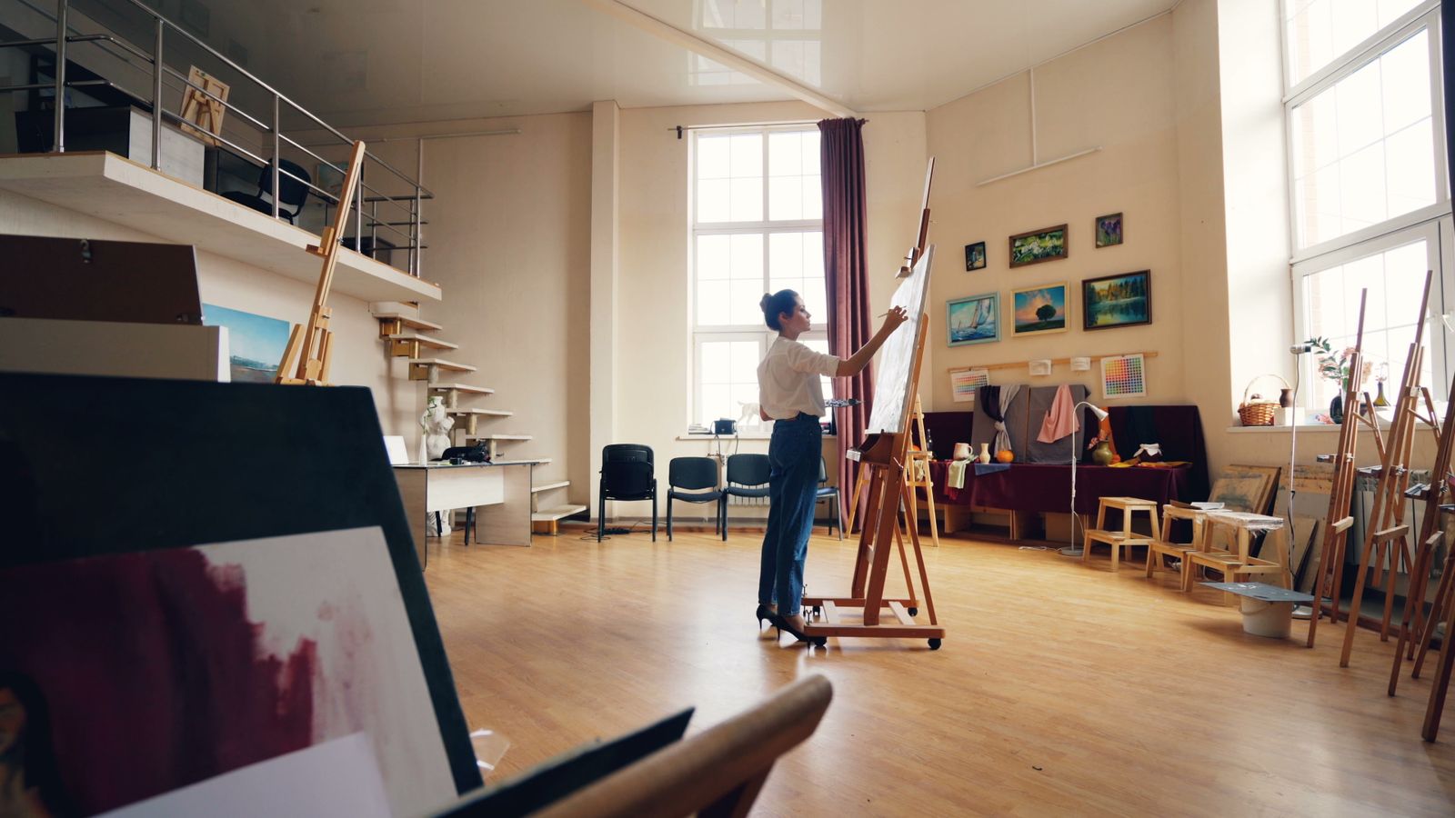 A woman painting on canvas in a bright, airy modern art studio.