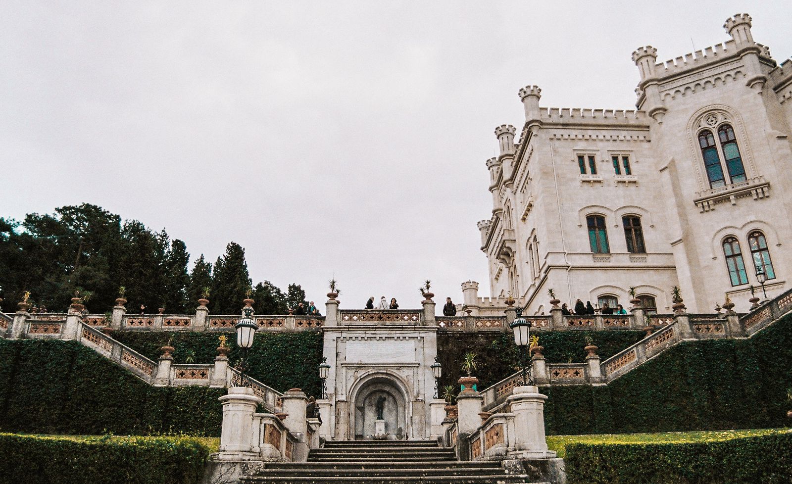 Majestic Italian castle facade with elaborate staircase, surrounded by lush gardens and architecture.