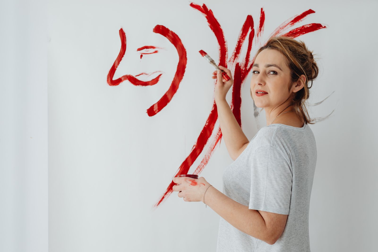 Female artist painting an abstract portrait on canvas with bold red strokes.